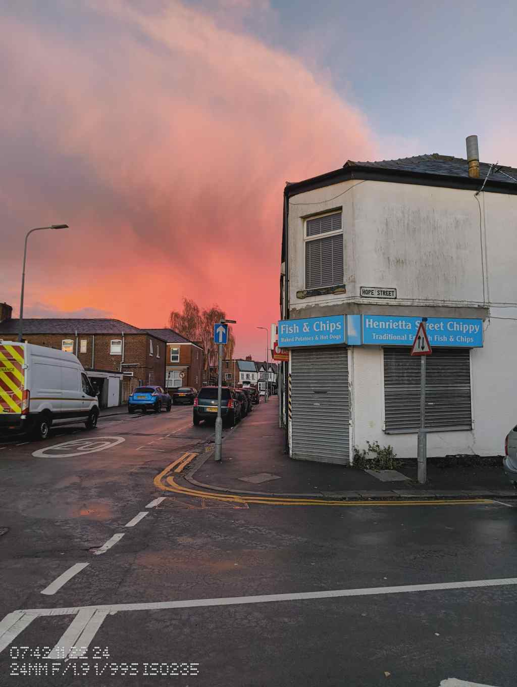 A view of Hope Street in Leigh during sunrise, with a dramatic pink and orange sky framing a traditional fish and chip shop on the corner.